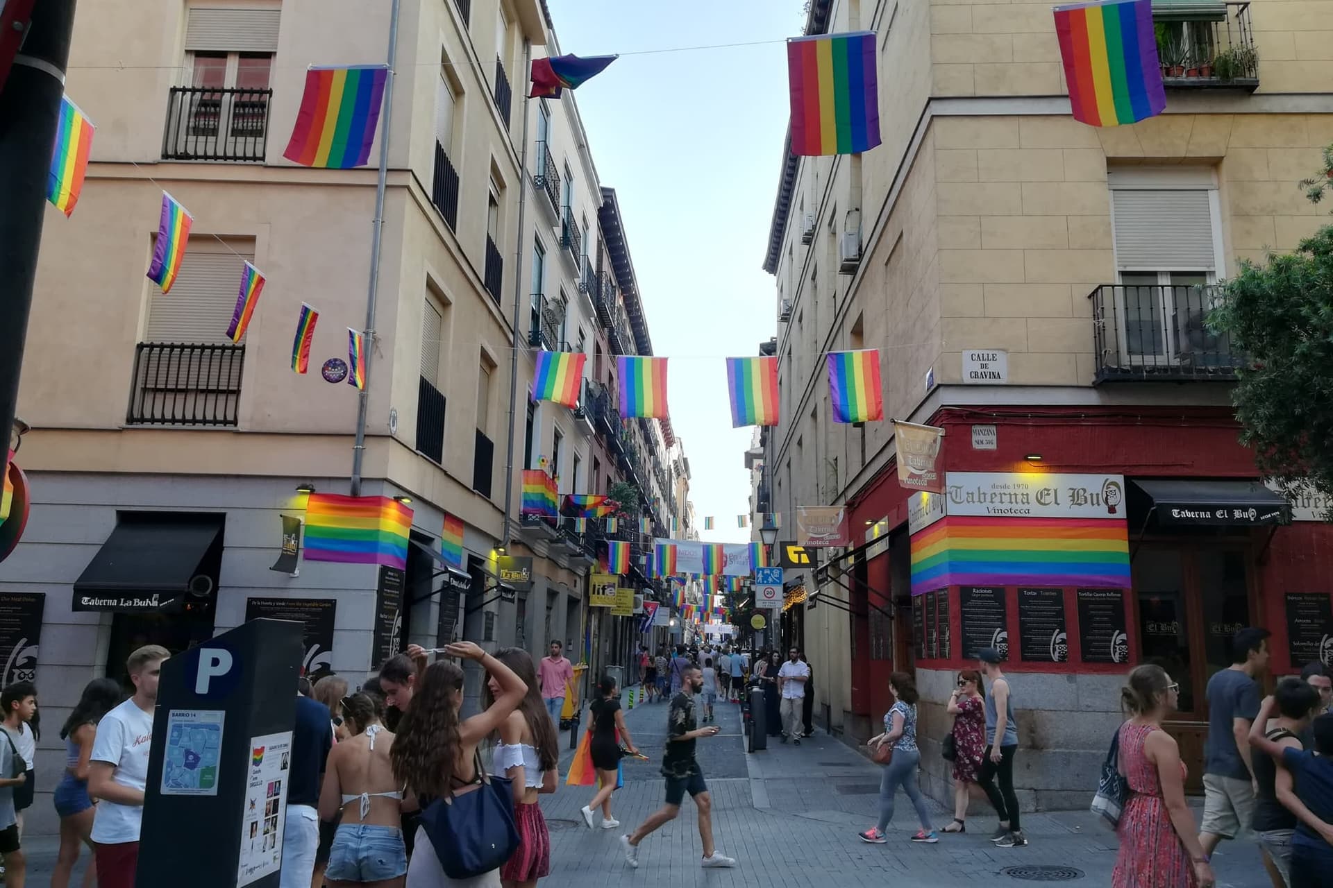 A busy street in Madrid's Chueca neighbourhood filled with people and rainbow flags during Pride.