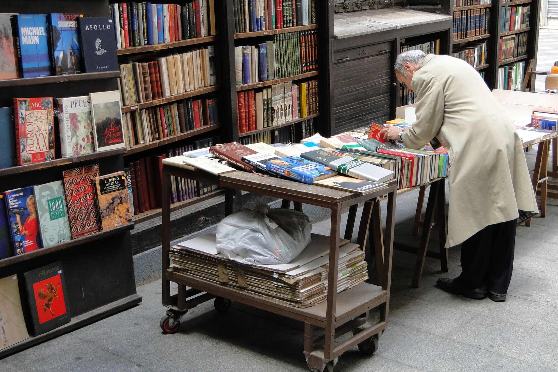 A customer browsing a second-hand bookstall in Madrid, books stacked to the roof of the kiosk.