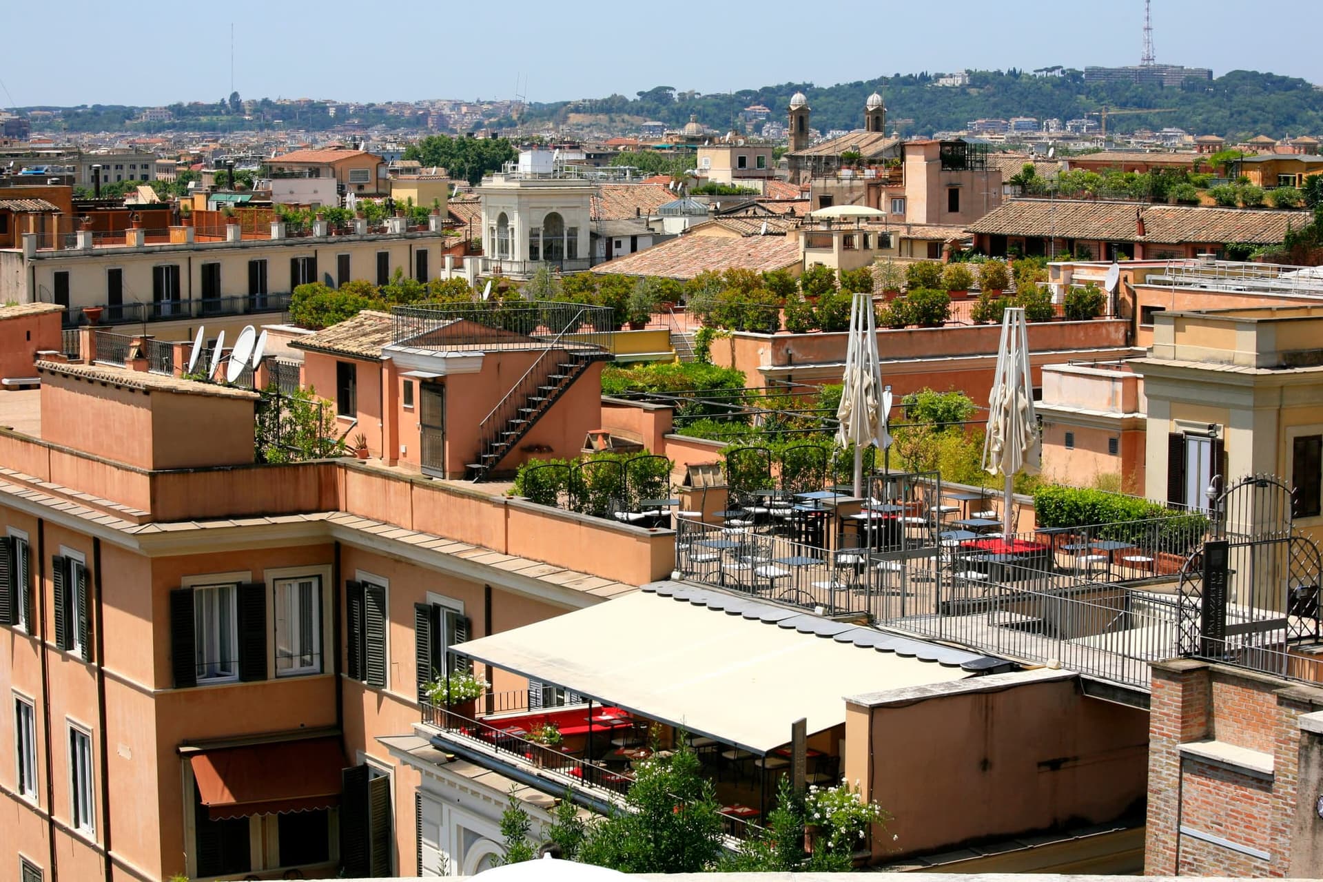 Roof terraces in Rome crowded with potted plants and small trees, seen across the tiles.