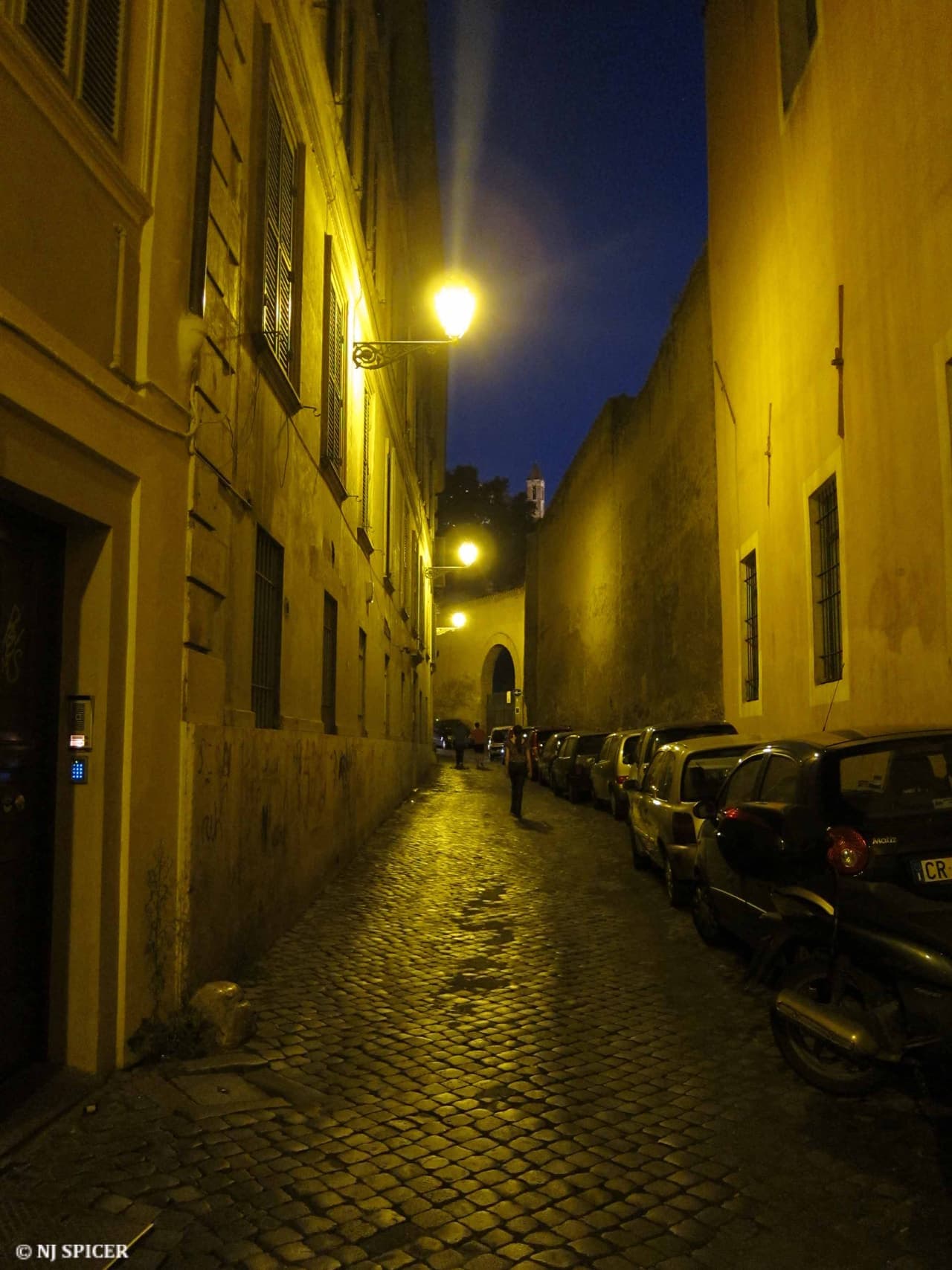 A narrow Trastevere lane with ivy climbing the ochre walls and scooters parked along one side.